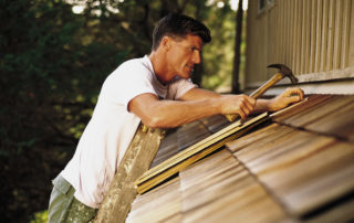 Man on ladder hammering roof